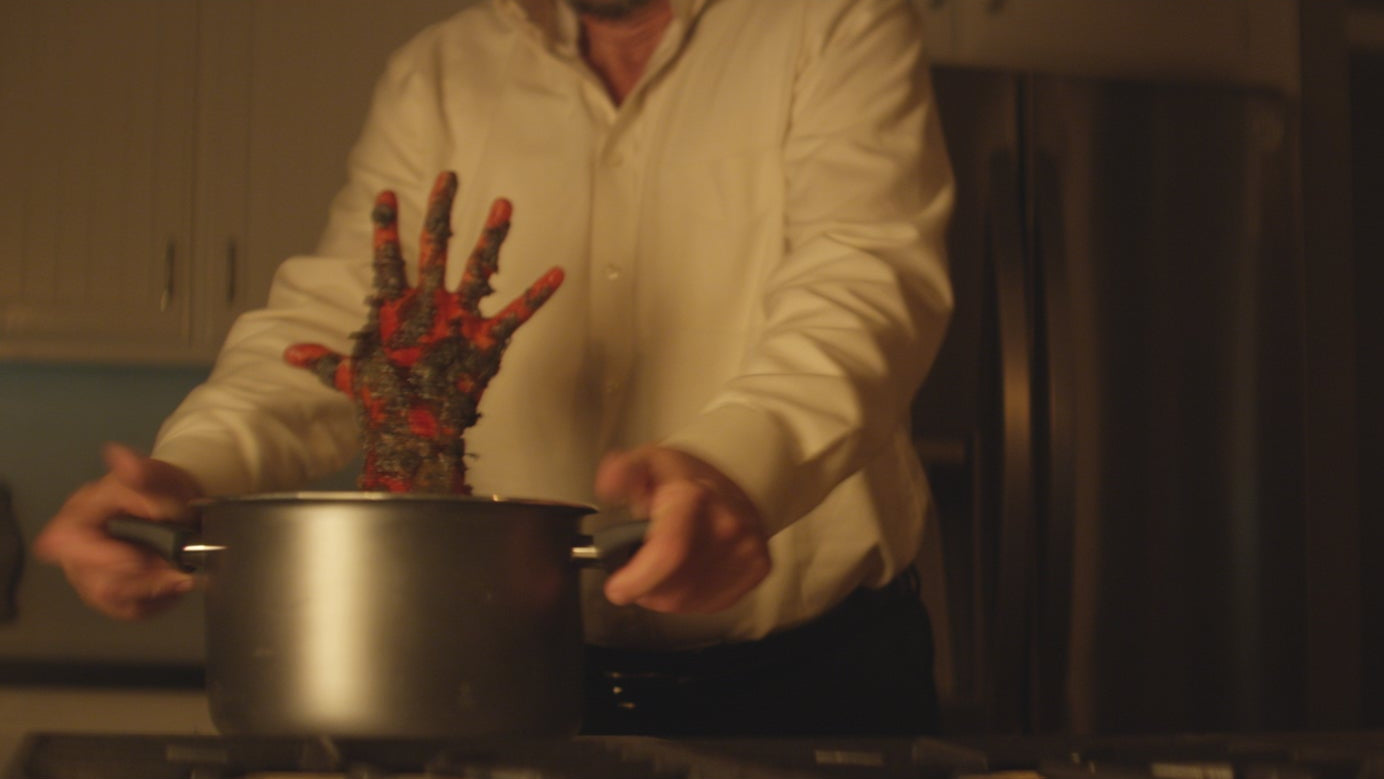 Person holding a pot with a hand with red and black patterns on a stove
