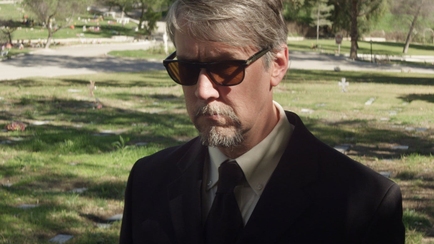 Man wearing sunglasses and a dark suit in a park setting