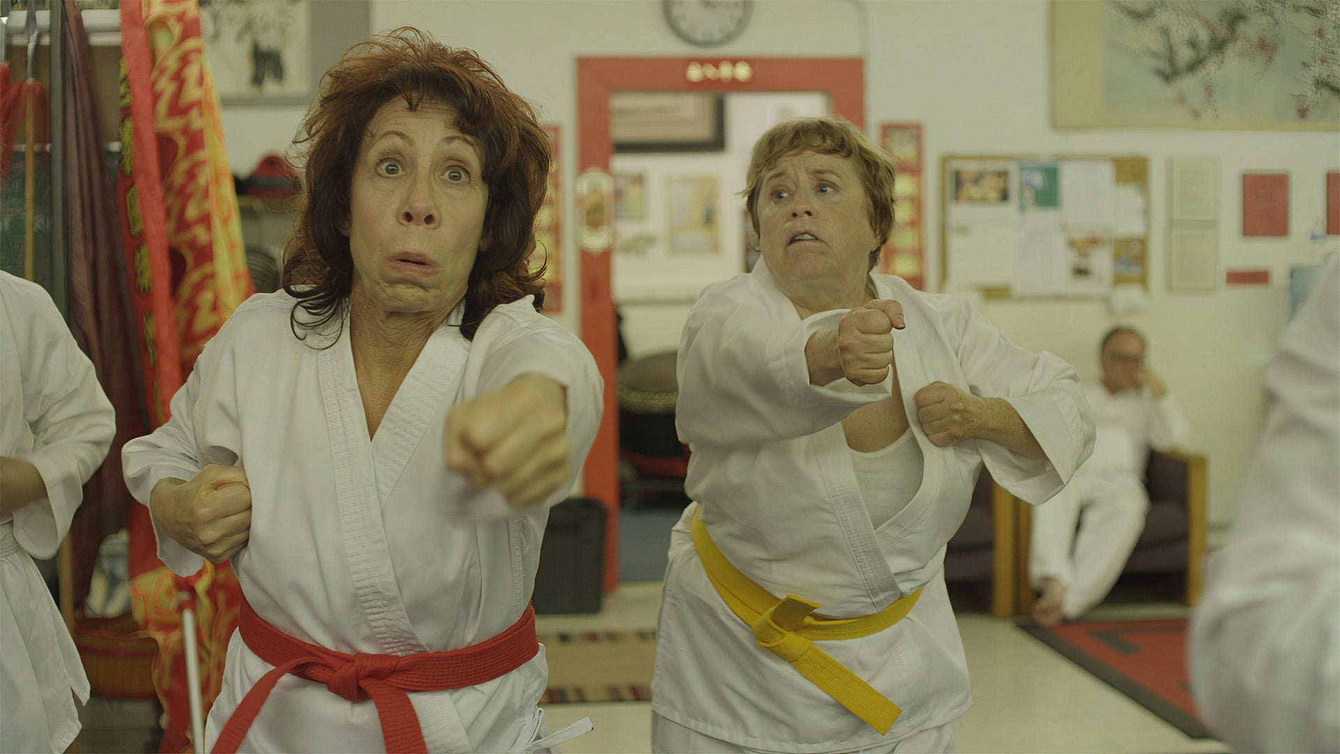 Two women in martial arts uniforms with red and yellow belts practicing in a dojo.