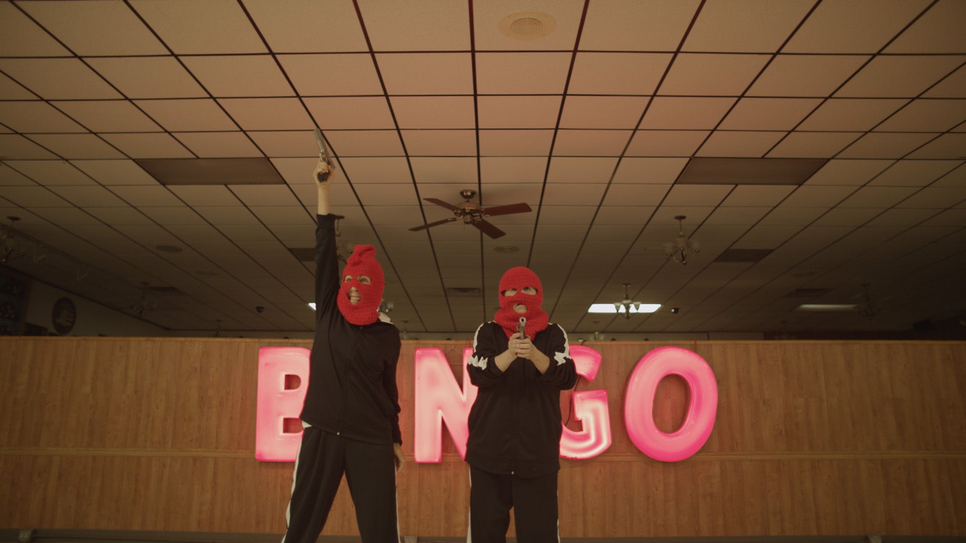 Two people wearing red masks in a Bingo hall with 'Bingo' sign visible.