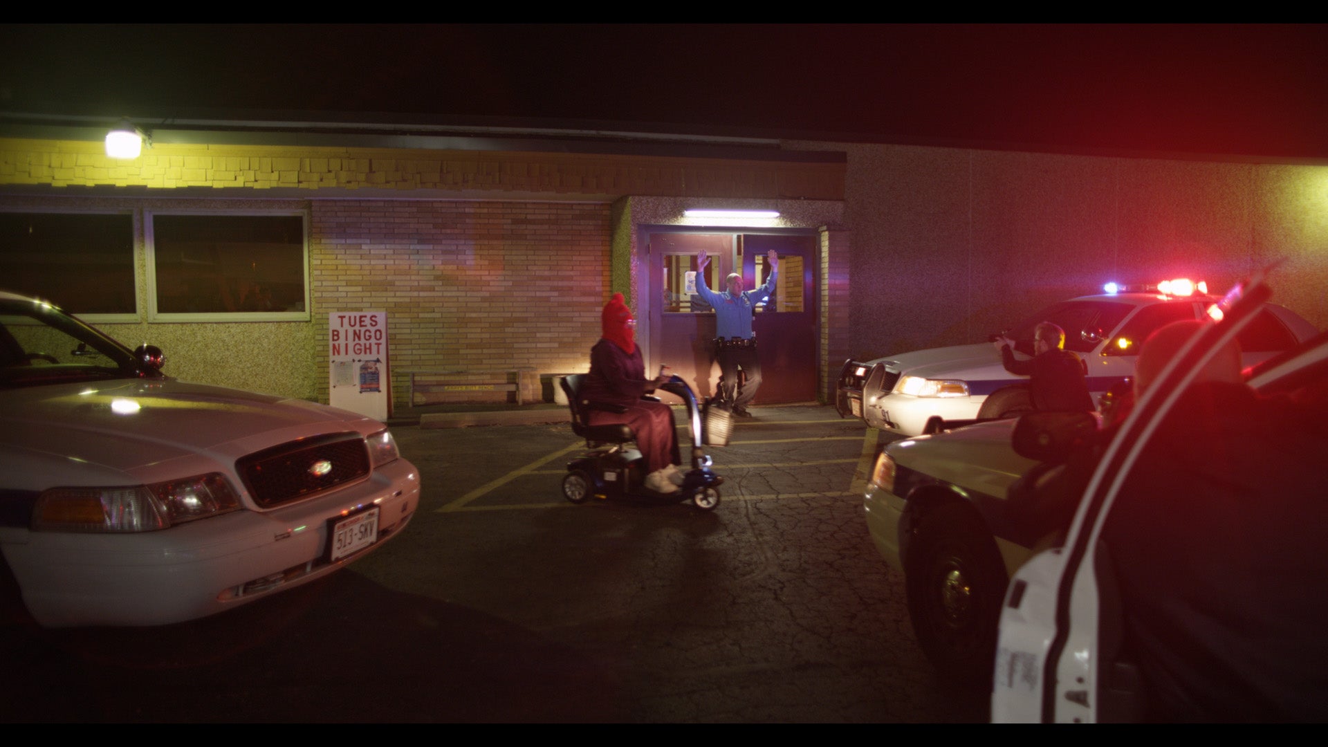 Person in a wheelchair being assisted by a police officer in a parking lot at night.