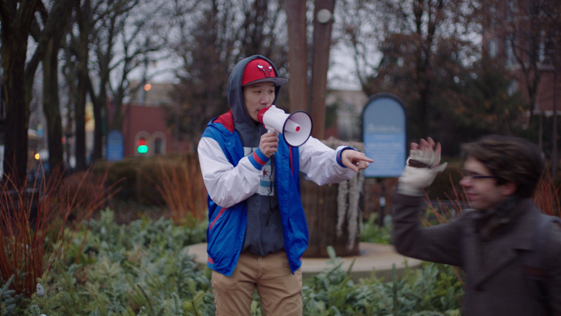 Person holding a megaphone in an outdoor setting with another person in the background.