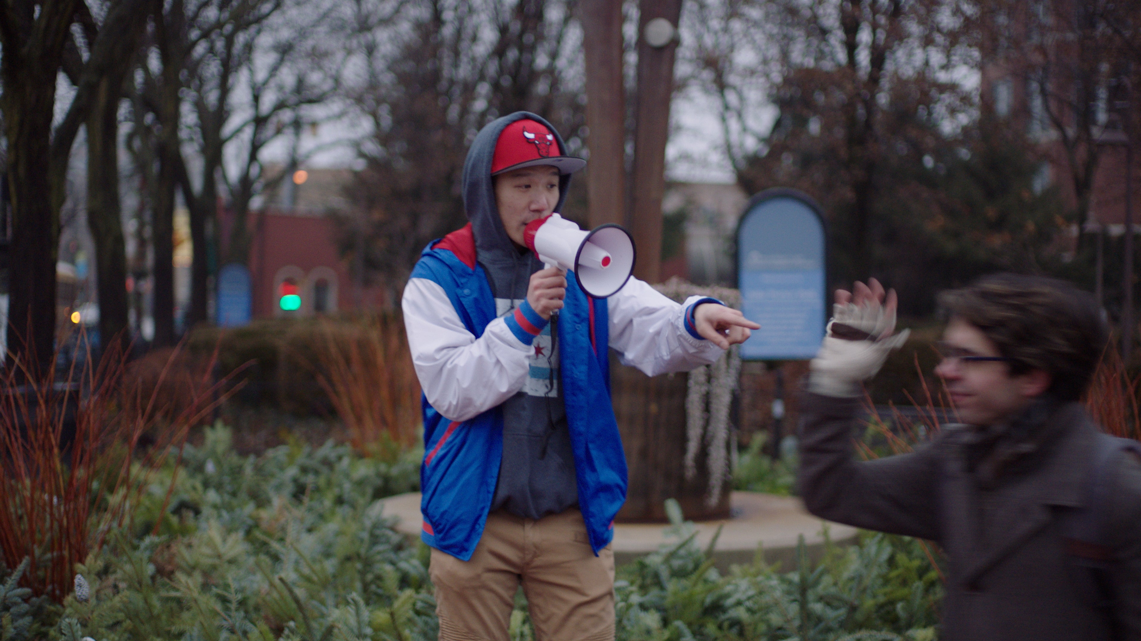Person holding a megaphone in an outdoor setting with another person in the background.