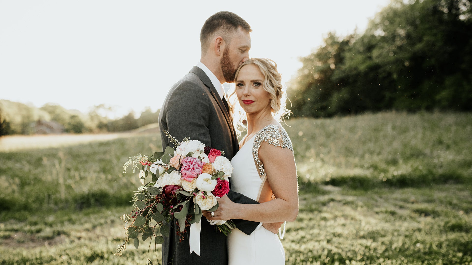 Couple on their wedding day in a field with a bouquet of flowers.