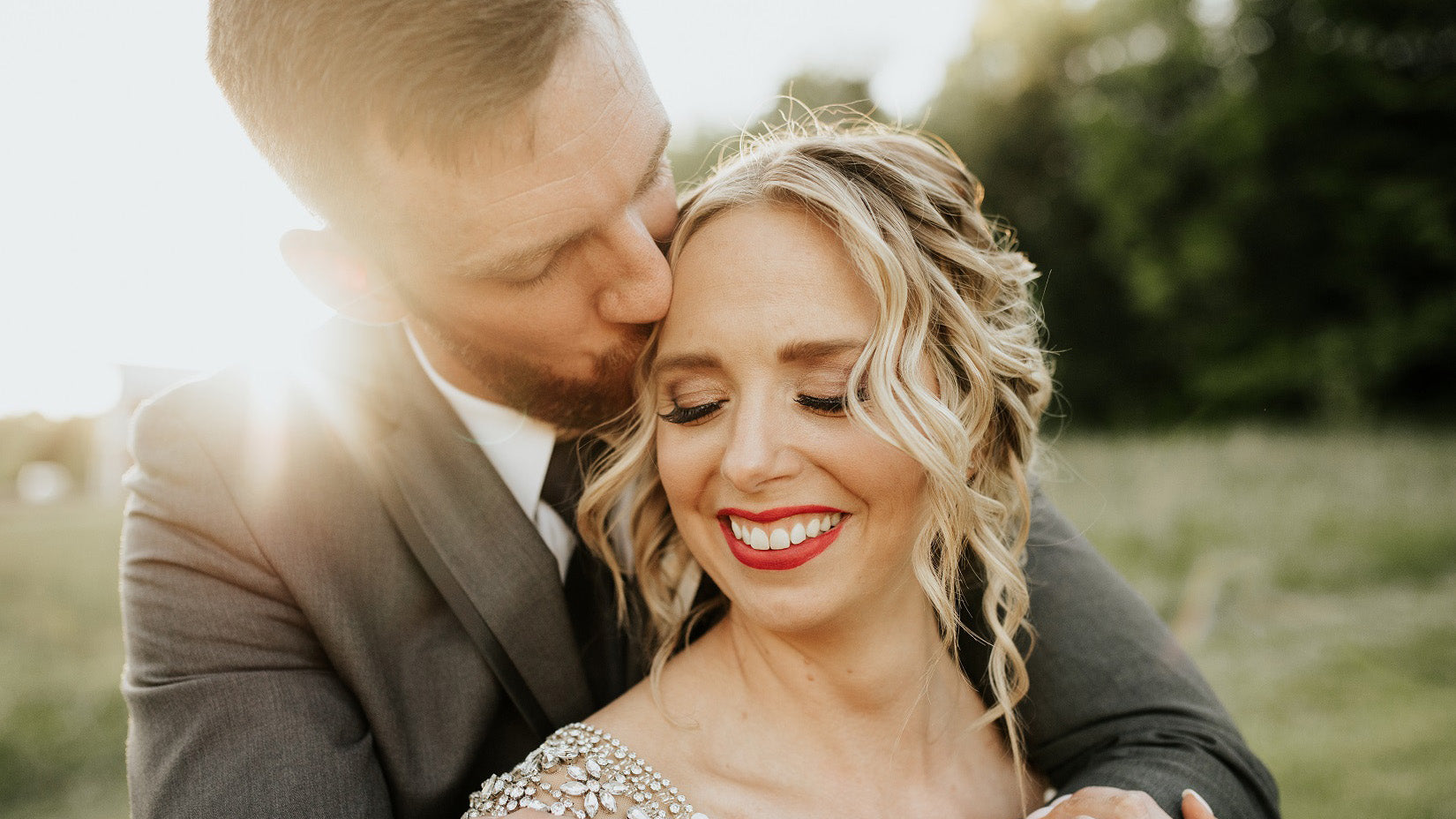 Man and woman embracing in a field with a warm, sunlit background