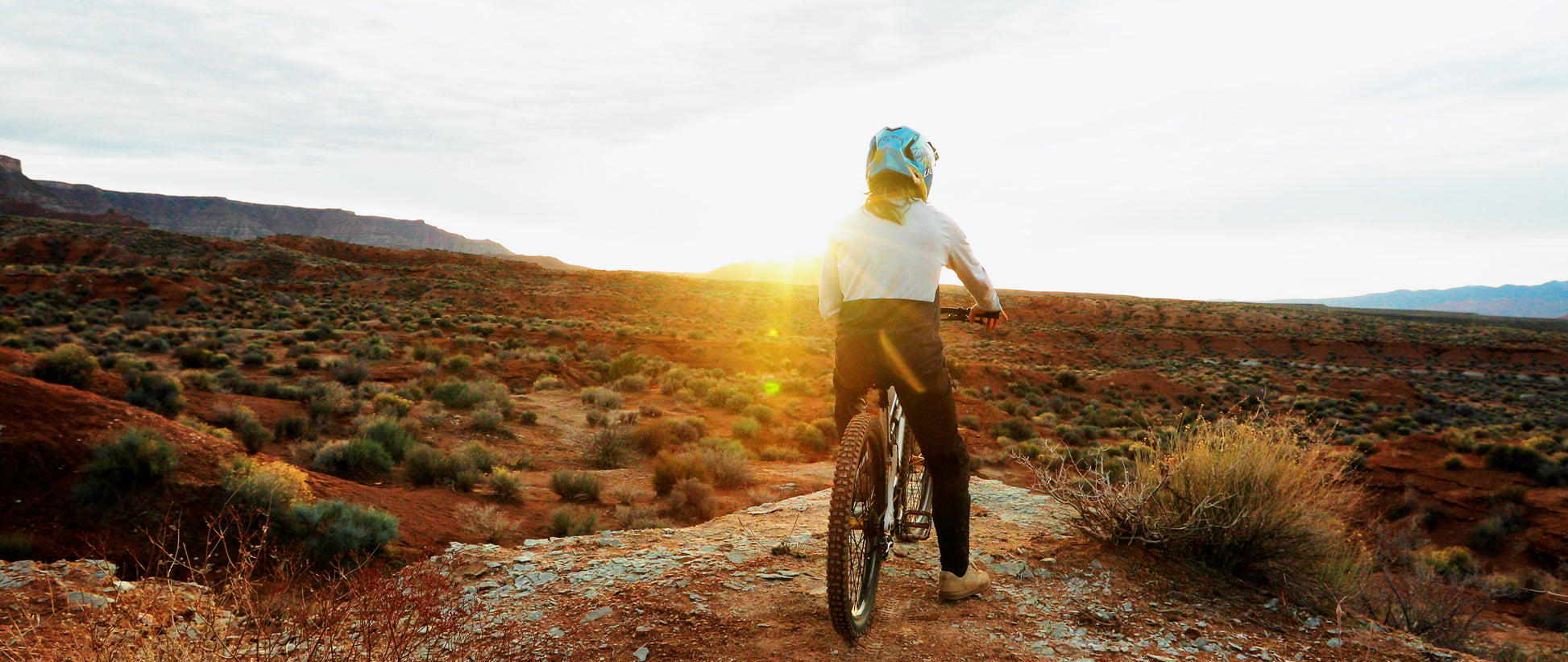 Person riding a bike on a desert trail with the sun setting in the background
