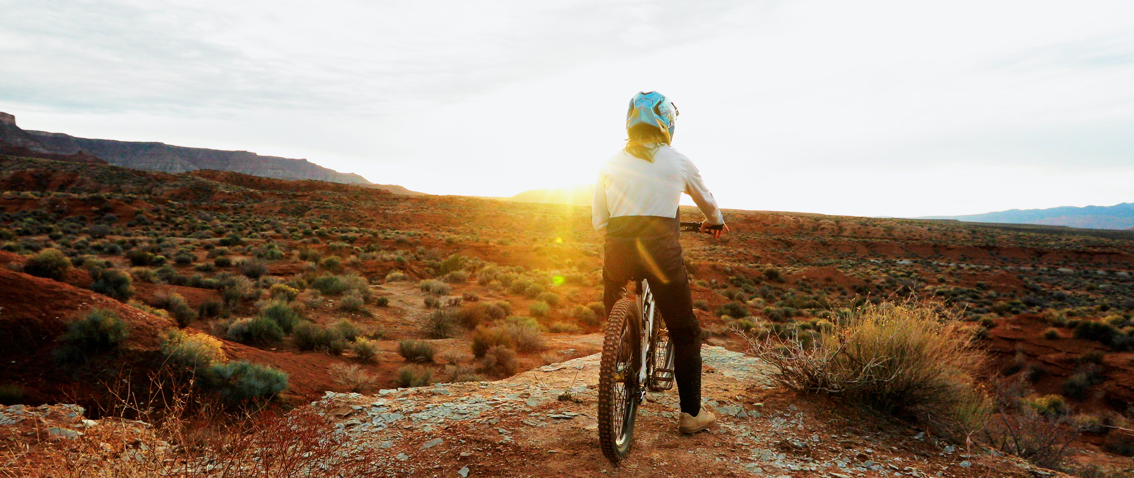 Person riding a bike on a desert trail with the sun setting in the background