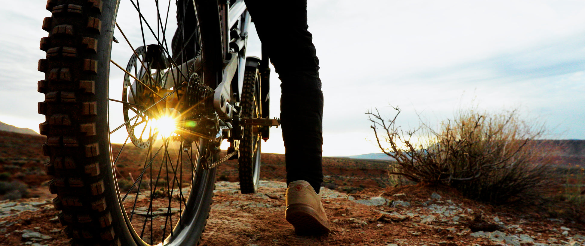 Person on a dirt bike in a desert landscape with a sunset.