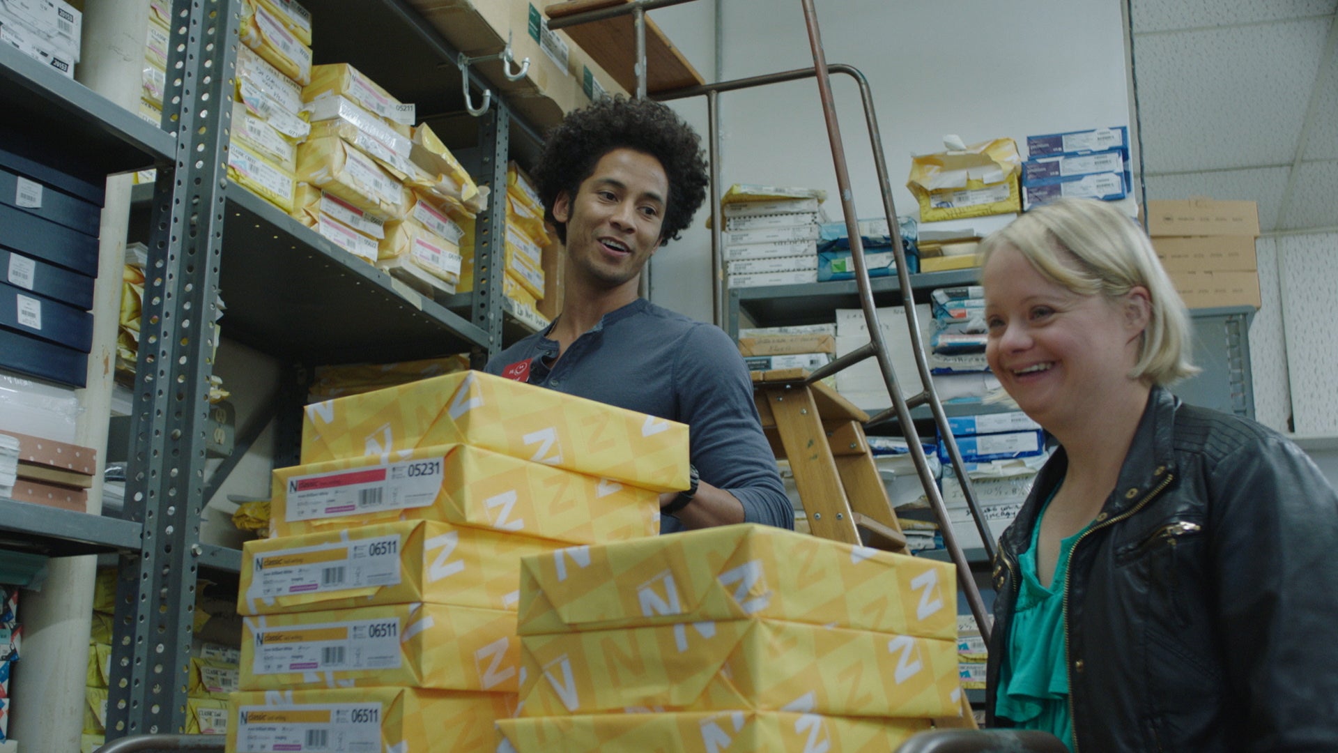 Two people in a warehouse with boxes and shelves.