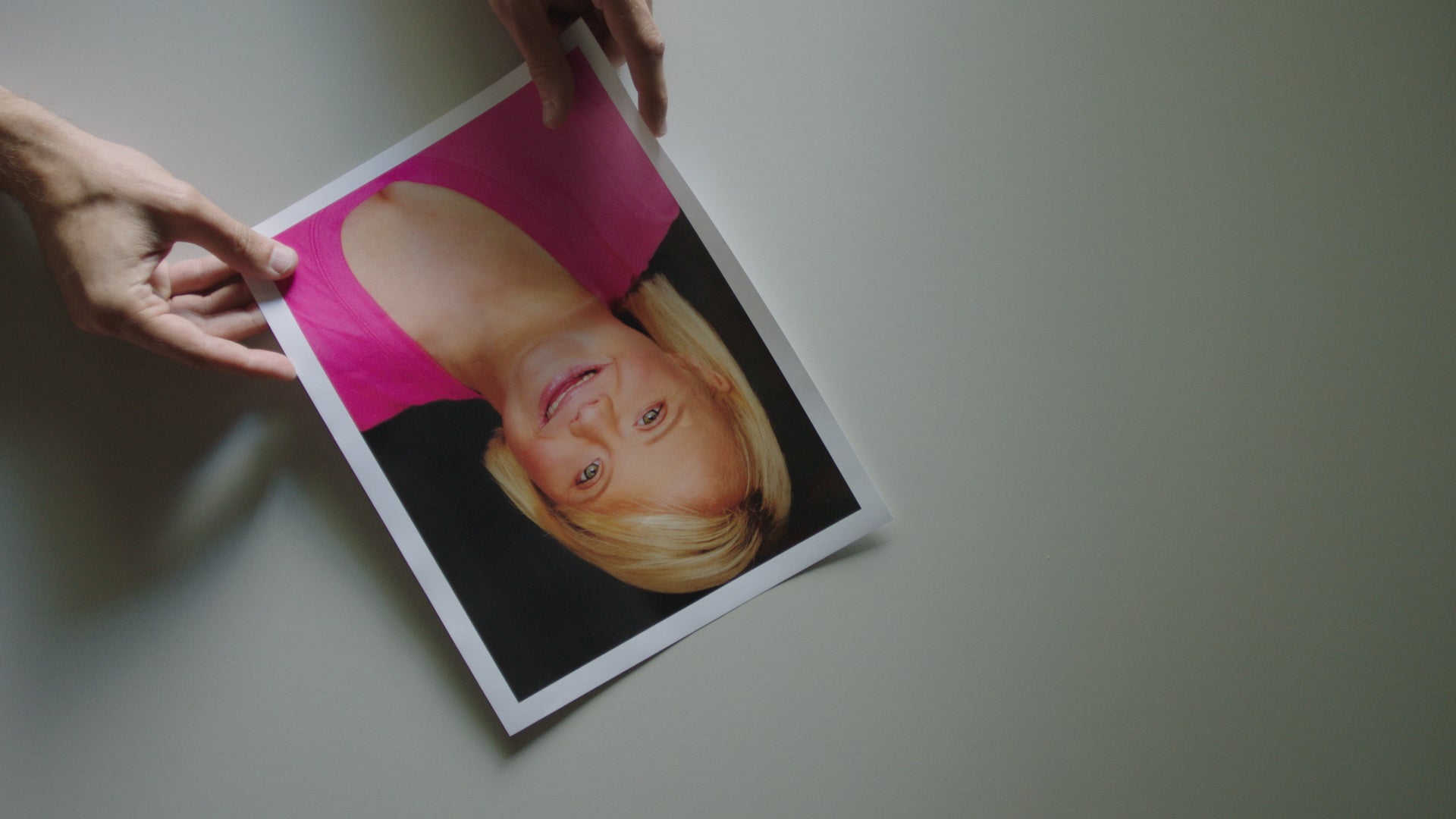 Person holding a photo of a woman with blonde hair on a plain background