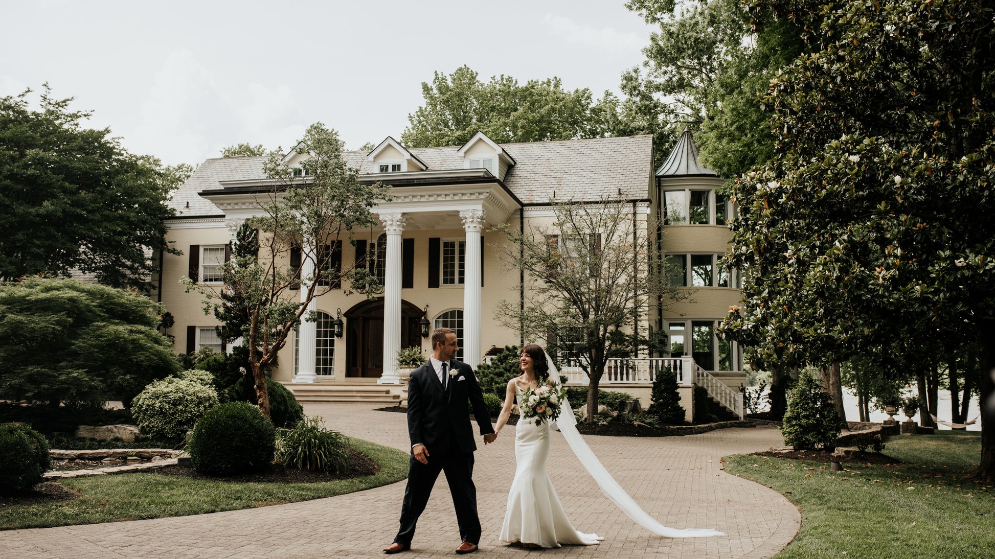 Wedding couple standing in front of a large, elegant house with columns.
