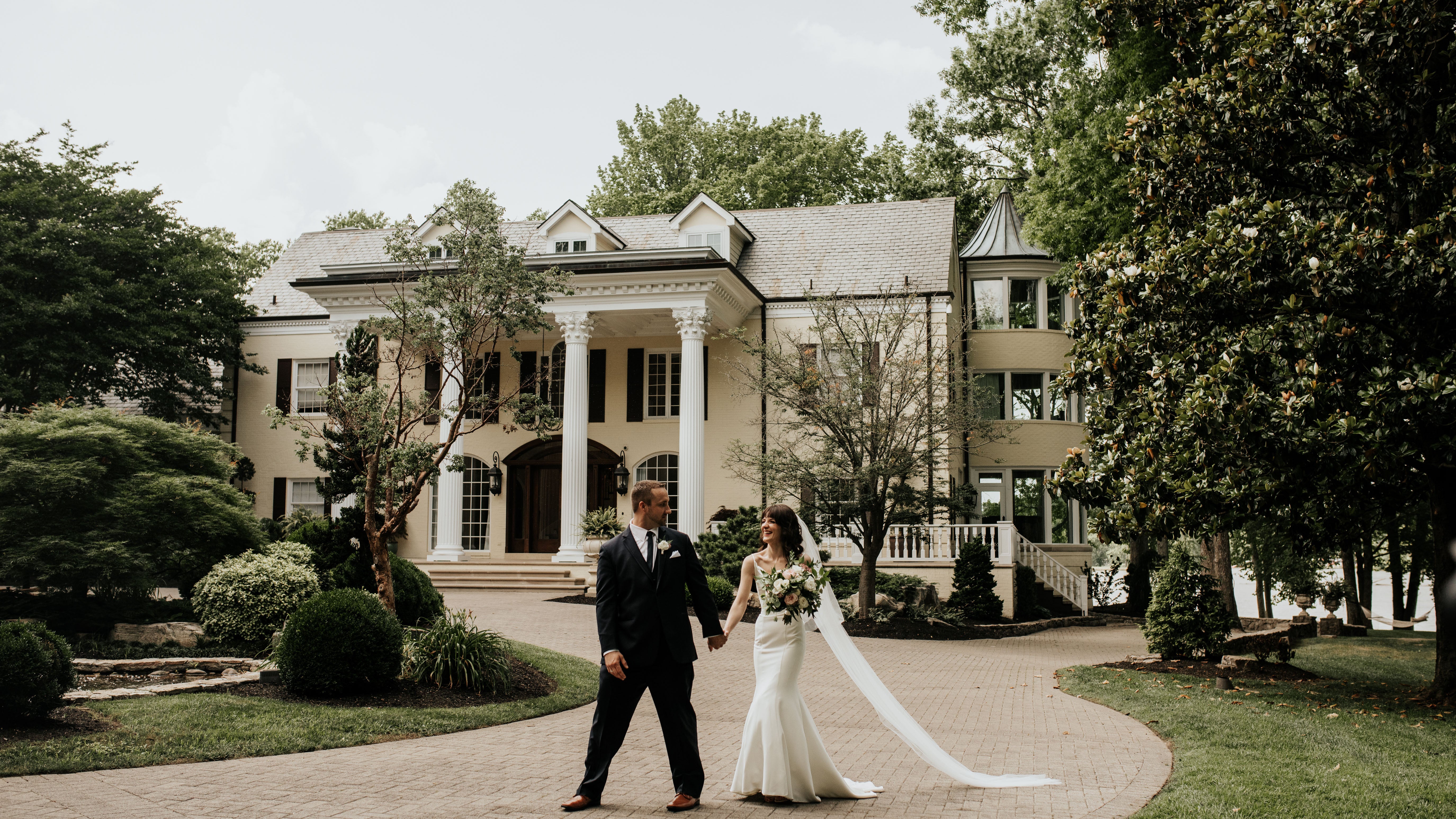 Wedding couple standing in front of a large, elegant house with columns.
