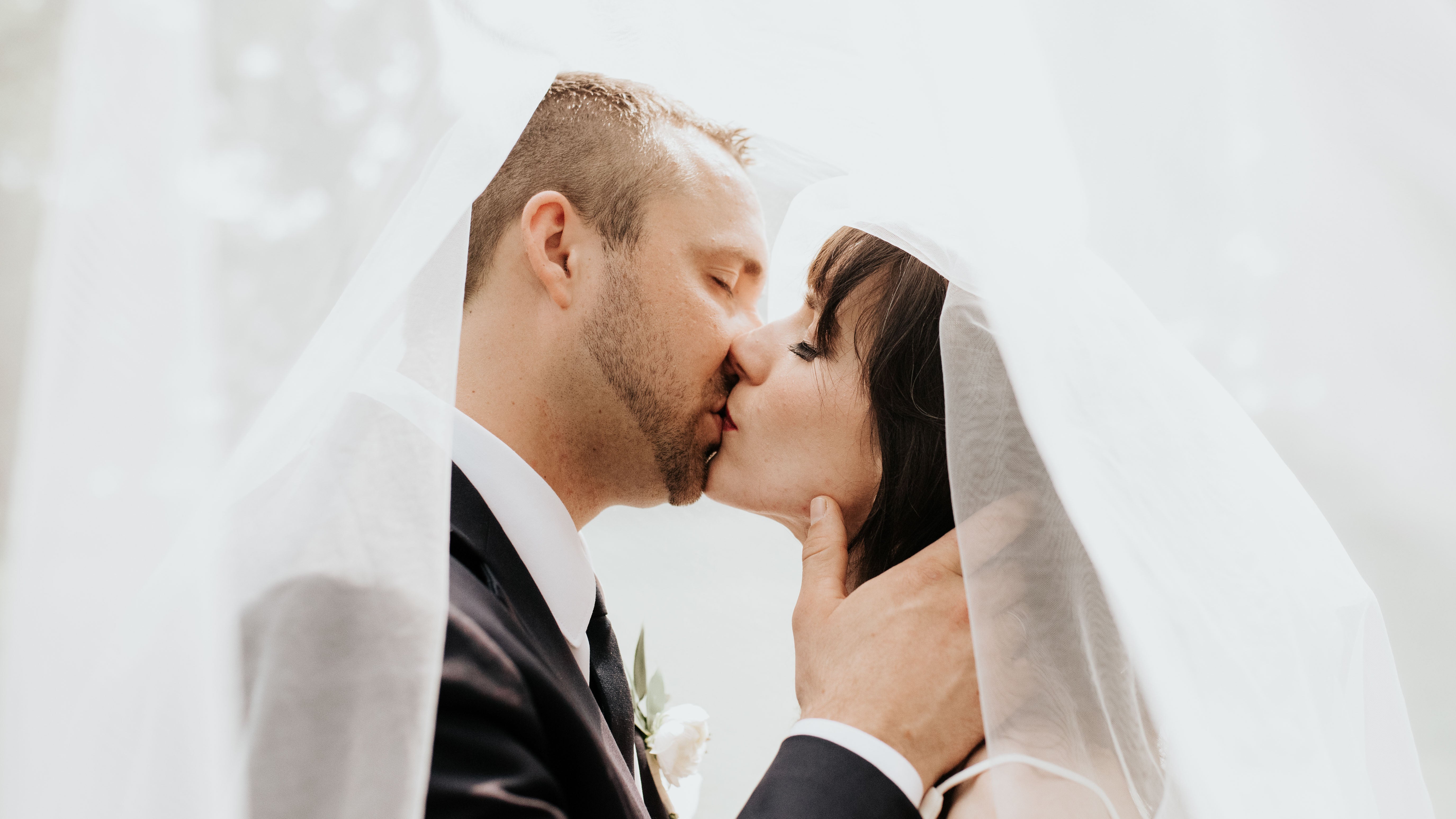 Couple sharing a kiss with a veil partially covering them against a white background