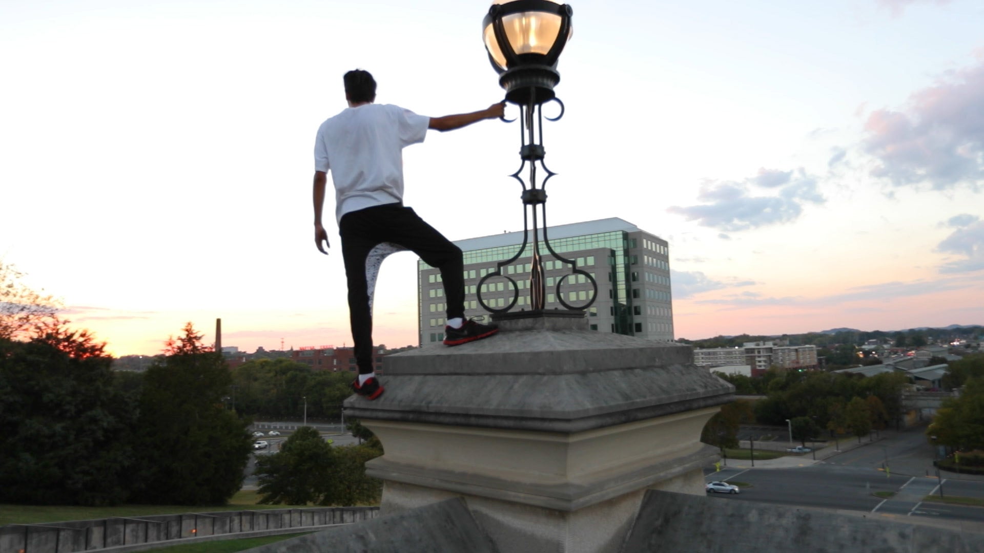 Person climbing a large outdoor light fixture with a cityscape in the background