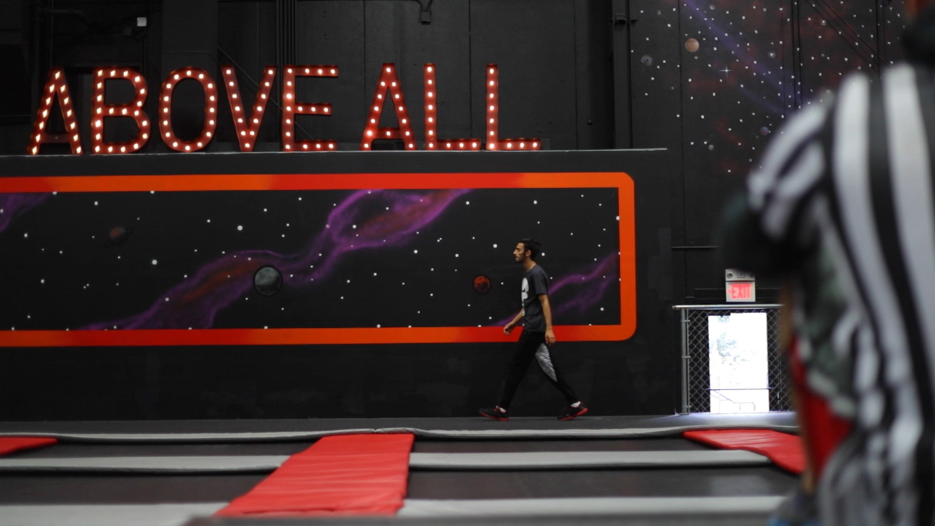 Person walking in a futuristic indoor setting with 'ABOVE ALL' neon sign.