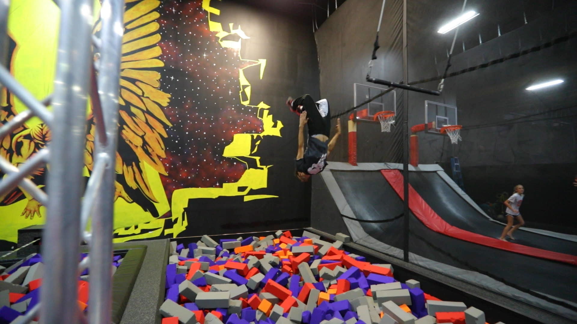 Indoor trampoline park with a person jumping off a ramp into colorful foam pits.