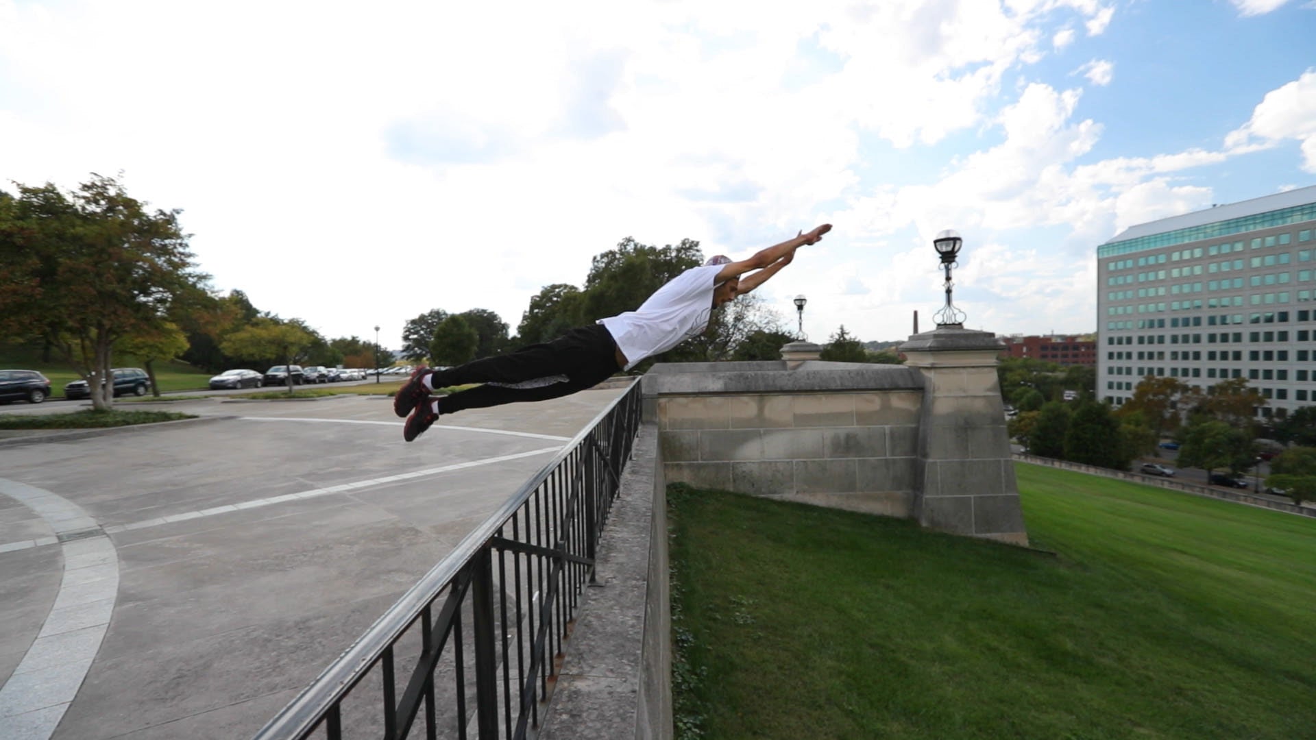 Person performing a backflip off a wall in an urban setting with cars and buildings in the background.