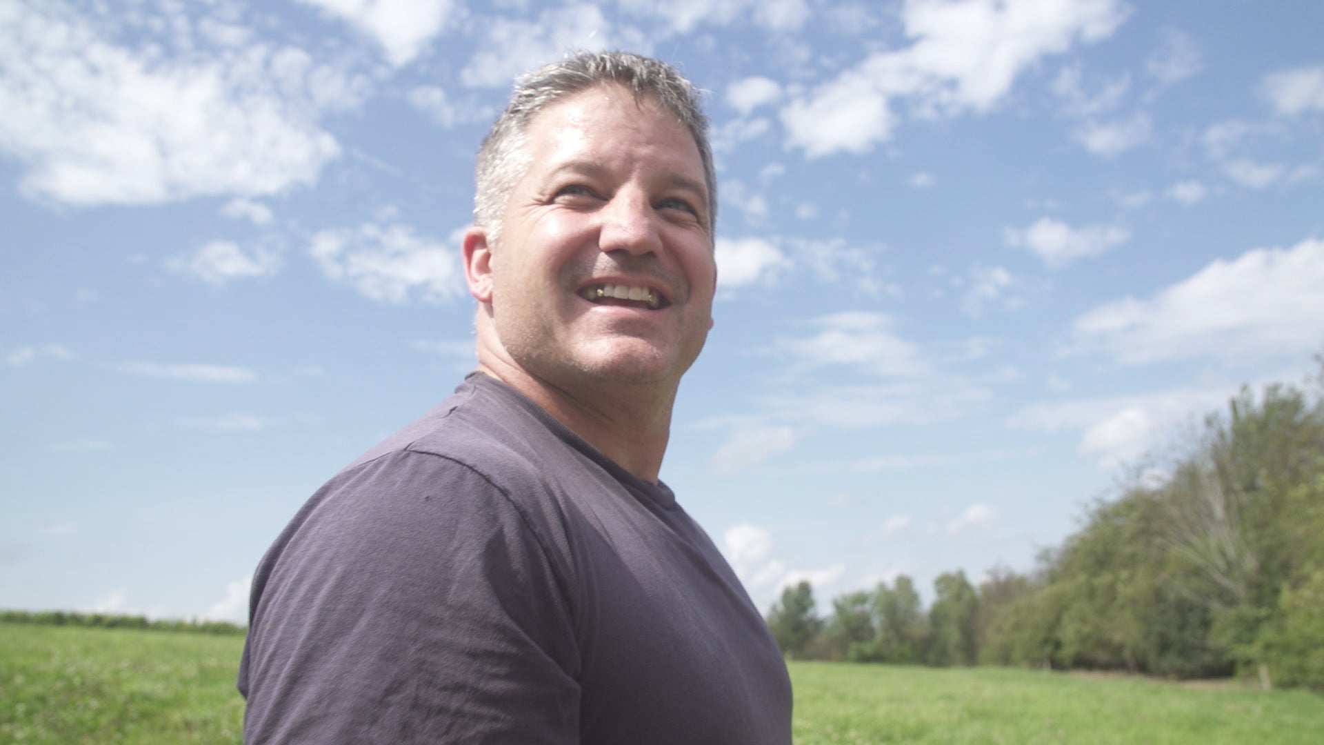 Man standing outdoors with a clear blue sky and green field in the background
