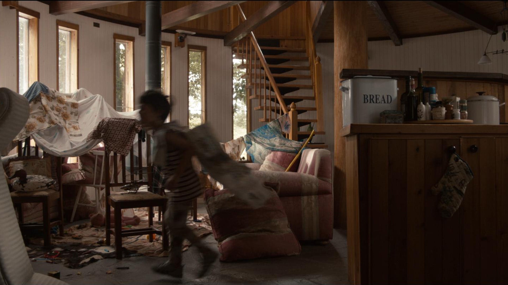 Person walking through a cluttered room with wooden furniture and a staircase.