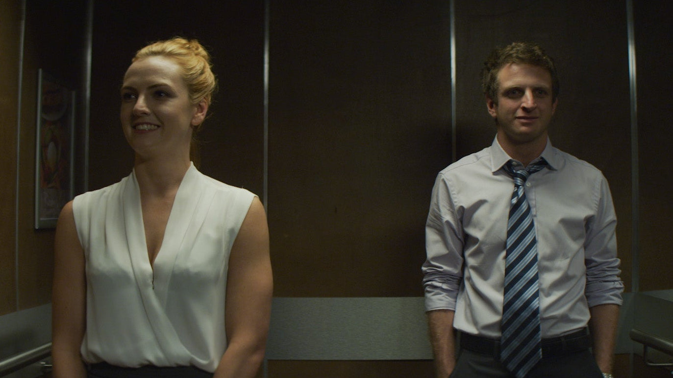 Two people standing in an elevator, one smiling and the other looking at the camera.