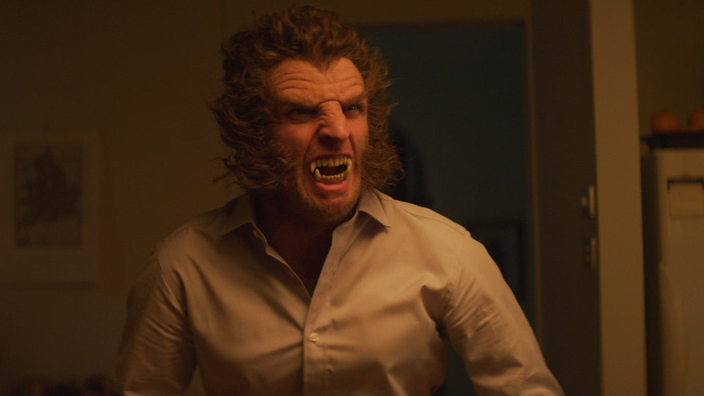 Man with a beard and long hair in a white shirt yelling in a room.