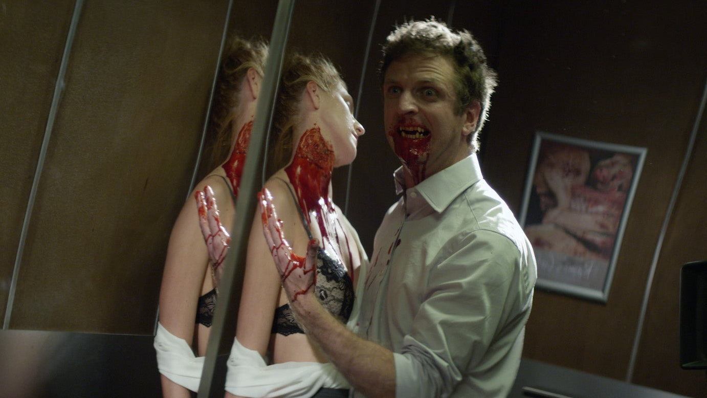 Man with bloodied face and woman with bloodied hands in a room with a mirror.