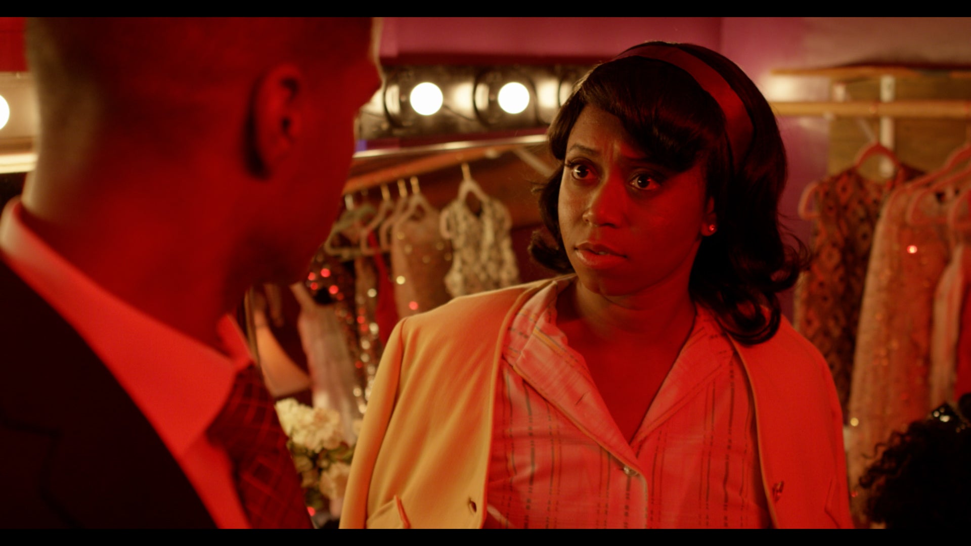 Woman in a pink jacket standing in a store with a man, surrounded by red lighting.