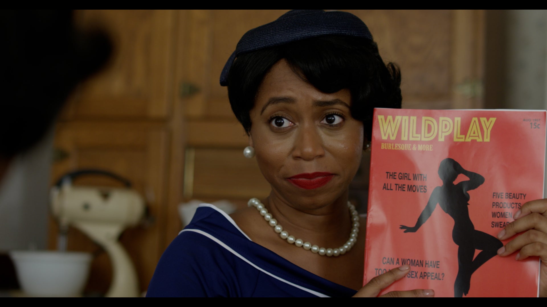 Woman holding a magazine titled 'Wildplay' in a kitchen setting