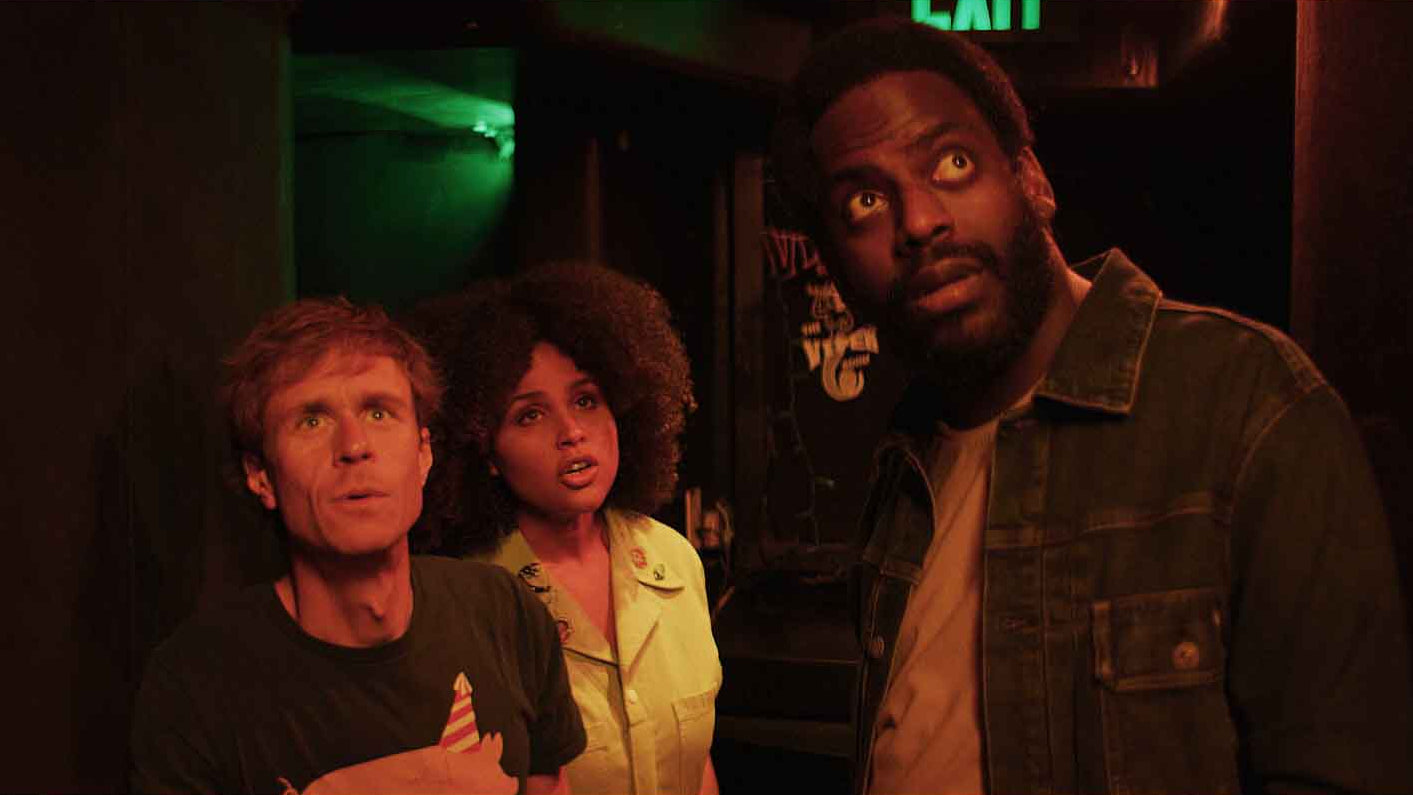 Three people standing in a dimly lit room with a green light in the background.