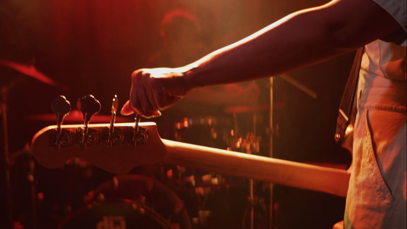 Person adjusting the tuning pegs of a guitar with a warm, red light.