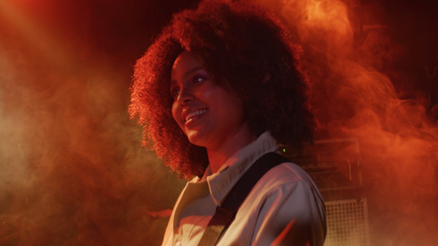 Person with curly hair in a red-lit environment with smoke