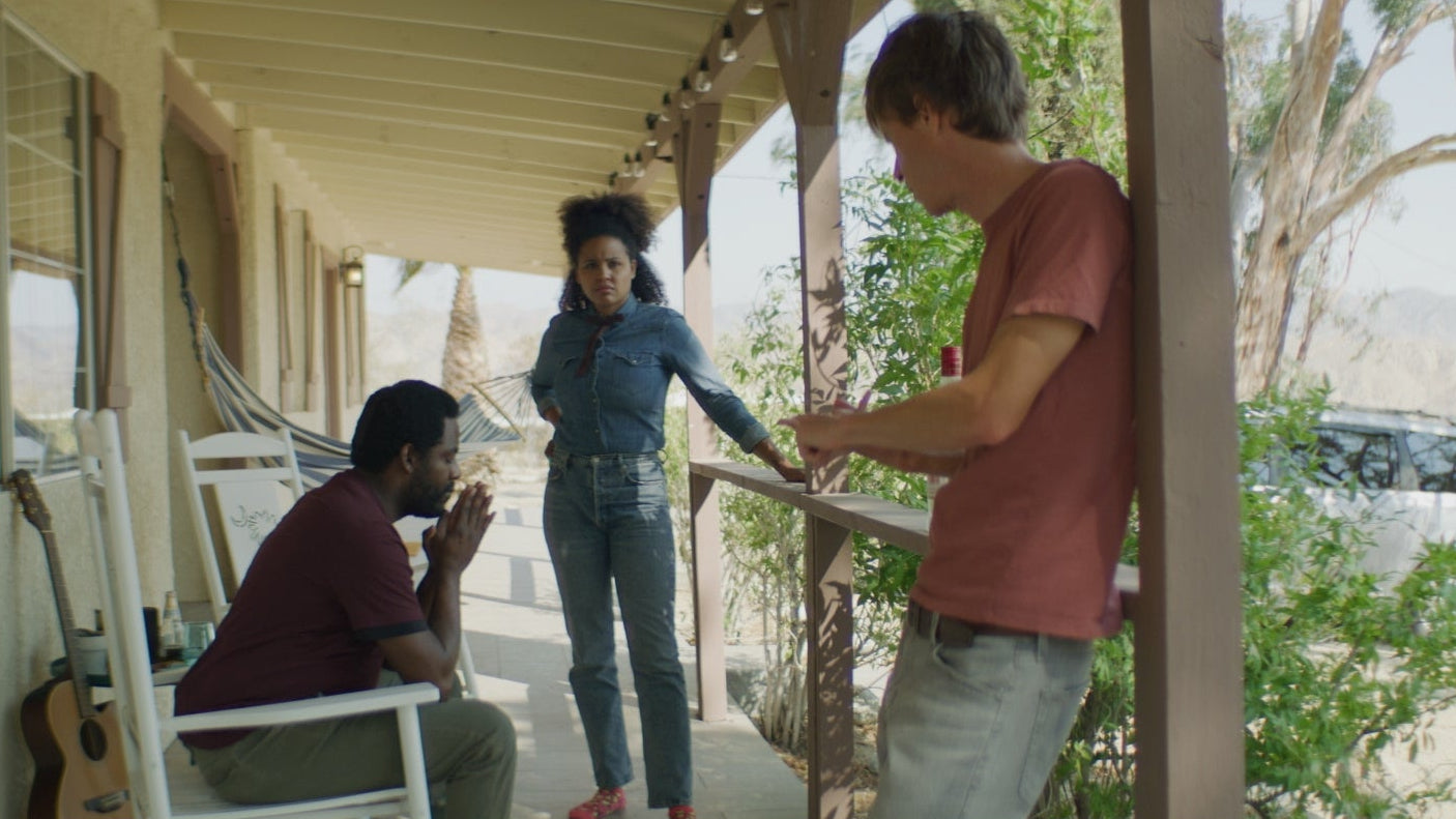 Three people on a porch with a house and car in the background