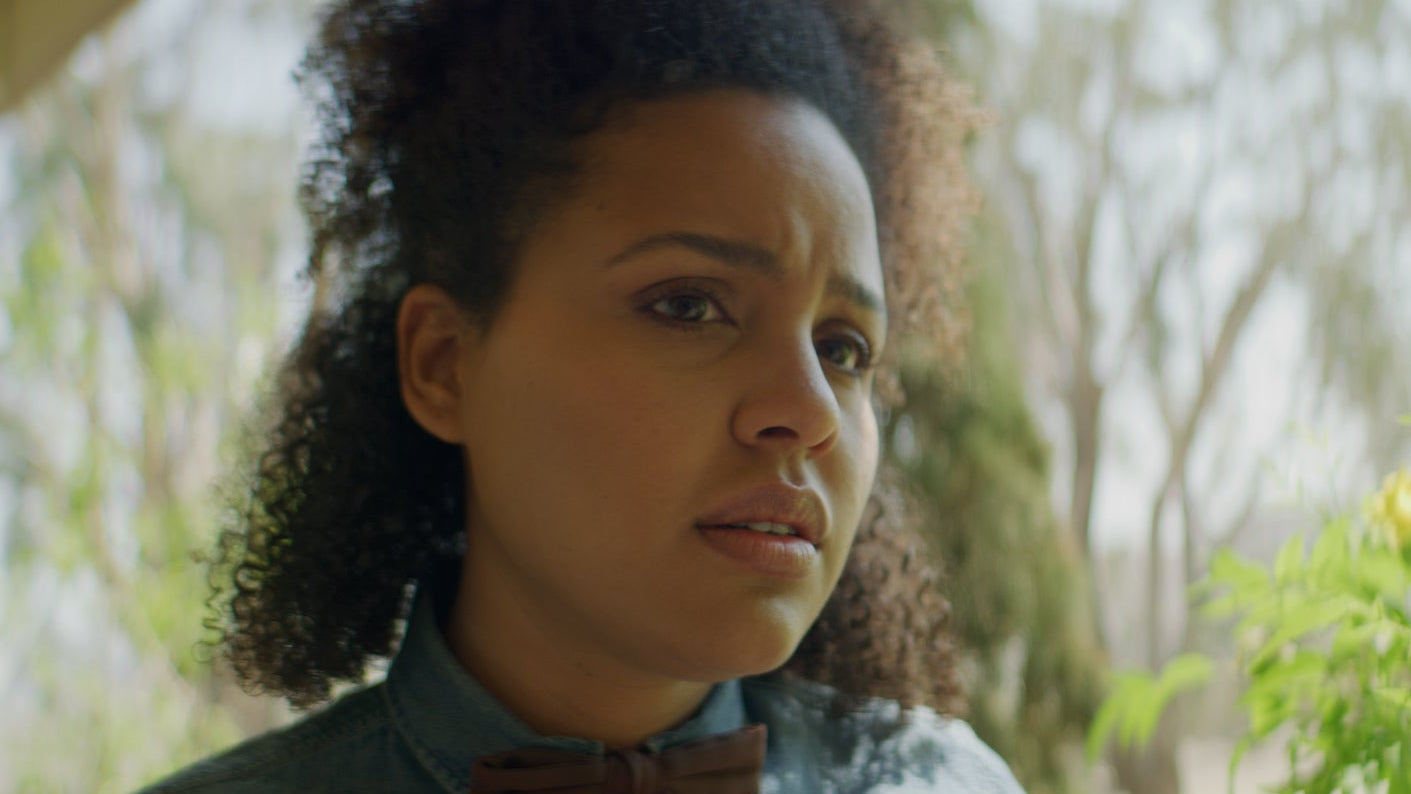 Woman with curly hair looking off to the side with a blurred natural background