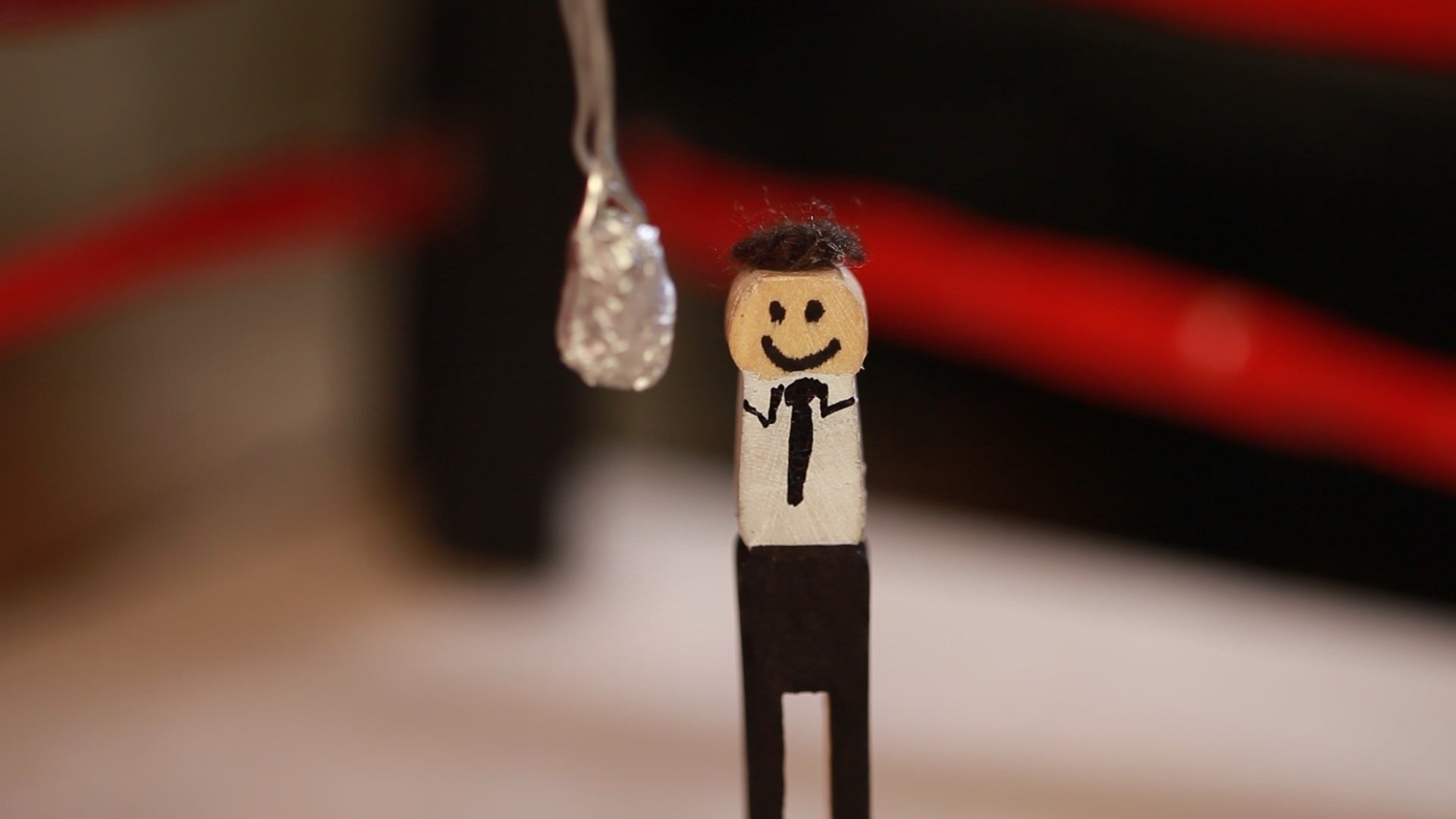 Wooden figure of a man with a suit and tie, holding a diamond ring, against a blurred background.