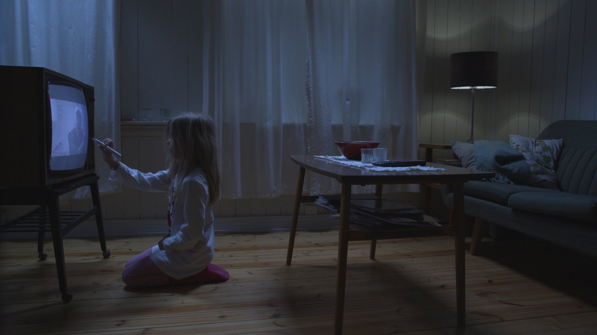 Person kneeling on the floor in a dimly lit room, pointing at an old television set.