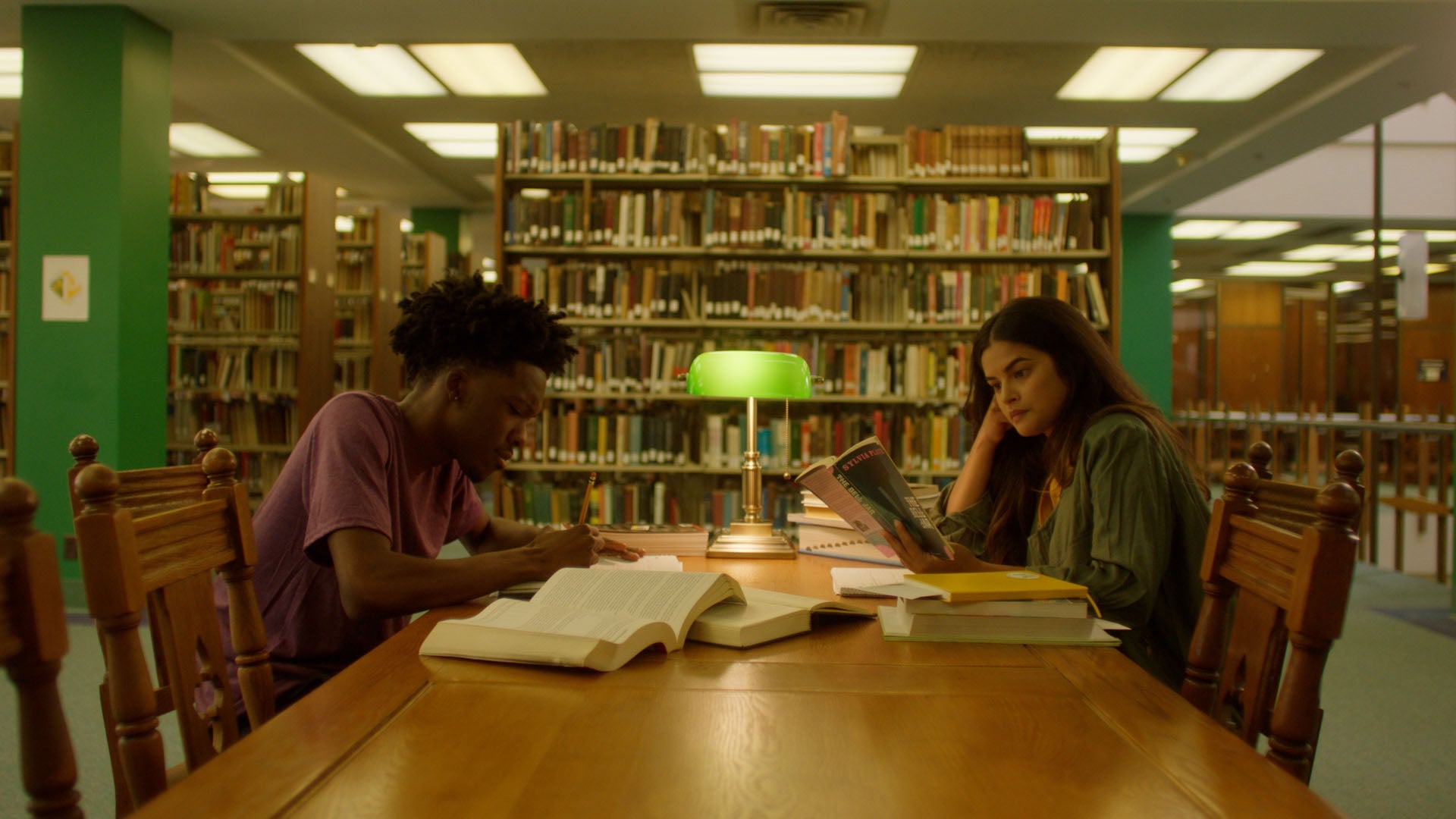 Two people studying in a library with bookshelves and a table.