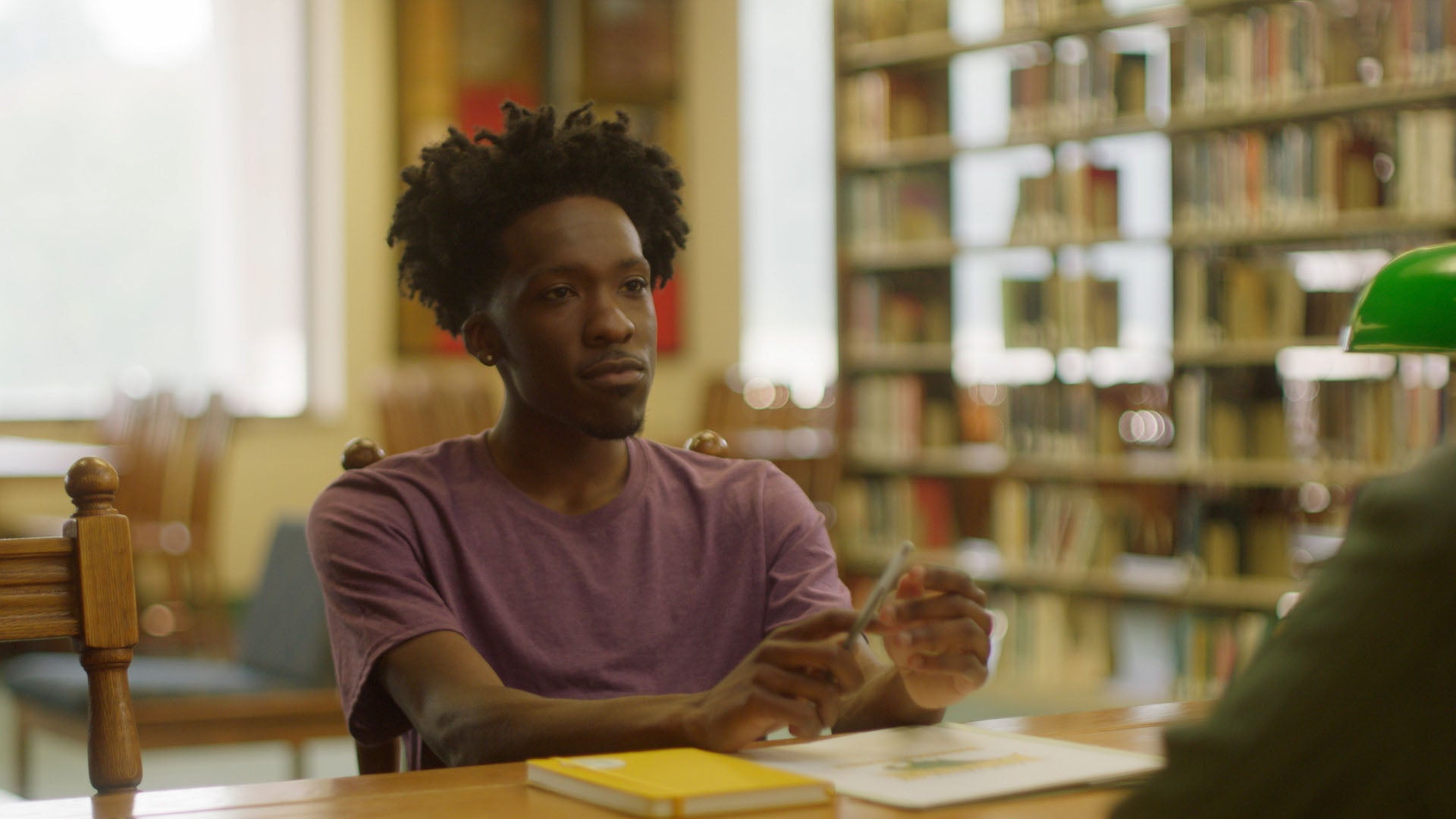 Man sitting at a table in a library holding a glass of water.